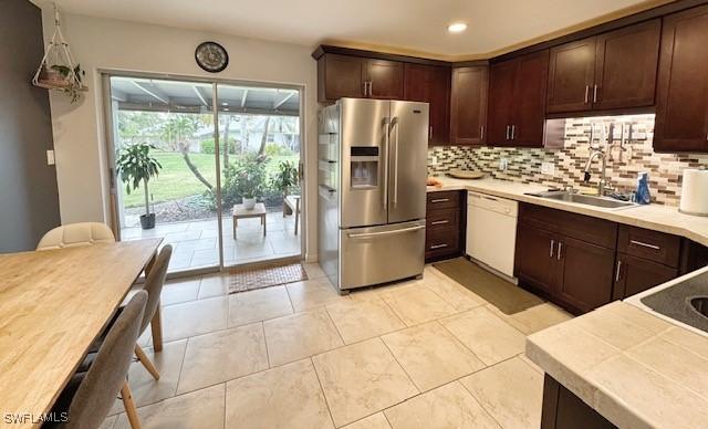 kitchen with sink, dishwasher, backsplash, dark brown cabinetry, and stainless steel refrigerator with ice dispenser