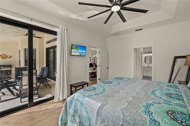 bedroom featuring ceiling fan, light hardwood / wood-style flooring, a tray ceiling, and ensuite bath