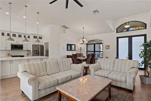 living room with french doors, ceiling fan with notable chandelier, hardwood / wood-style flooring, and high vaulted ceiling