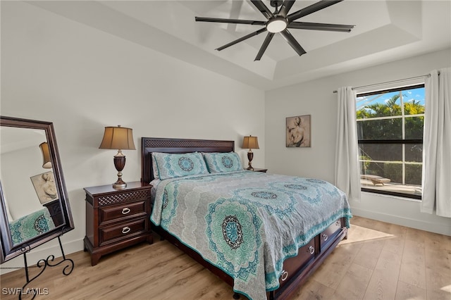 bedroom with a tray ceiling, ceiling fan, and light hardwood / wood-style floors