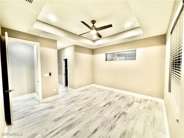 unfurnished room with ceiling fan, light hardwood / wood-style floors, and a tray ceiling