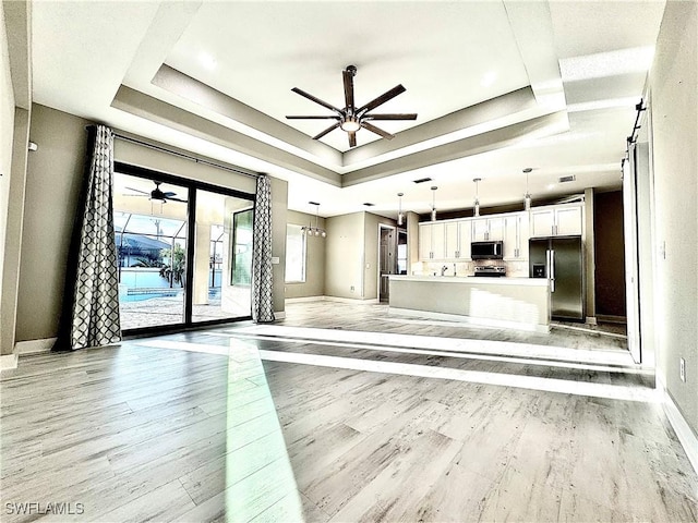 unfurnished living room featuring ceiling fan, sink, a tray ceiling, and light hardwood / wood-style floors