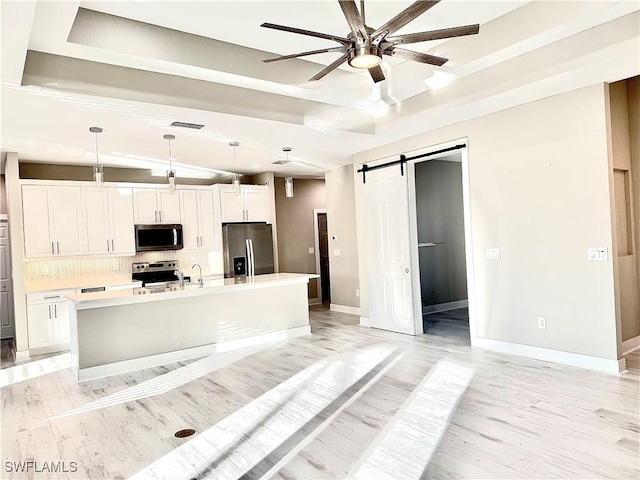 kitchen with appliances with stainless steel finishes, pendant lighting, an island with sink, white cabinetry, and a barn door