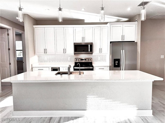 kitchen with white cabinetry, sink, hanging light fixtures, stainless steel appliances, and a center island with sink