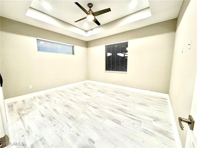 spare room with a tray ceiling, ceiling fan, and light wood-type flooring