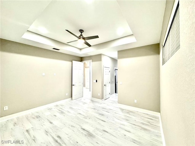 empty room with ceiling fan, a raised ceiling, and light wood-type flooring