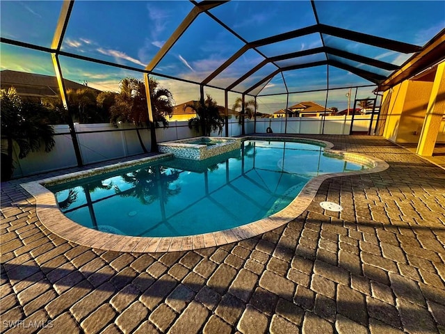 pool at dusk featuring an in ground hot tub, a patio area, and glass enclosure