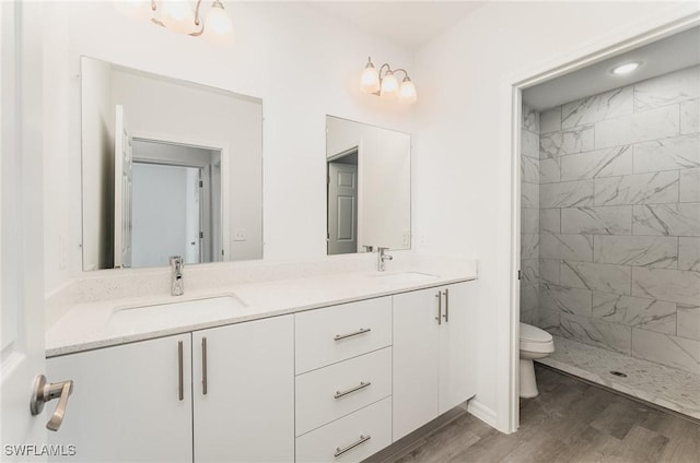 bathroom with hardwood / wood-style floors, vanity, toilet, and tiled shower