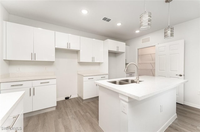 kitchen with white cabinetry, sink, light hardwood / wood-style flooring, an island with sink, and decorative light fixtures