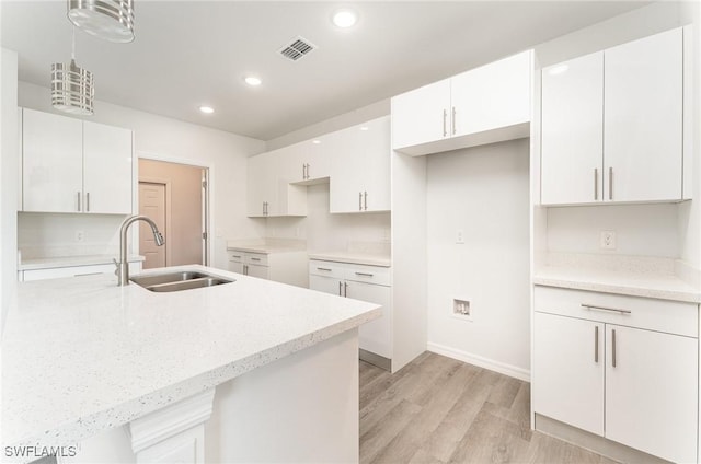 kitchen with white cabinets, pendant lighting, sink, and light hardwood / wood-style flooring