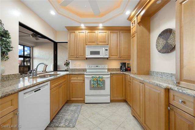 kitchen with light stone countertops, white appliances, a tray ceiling, and sink