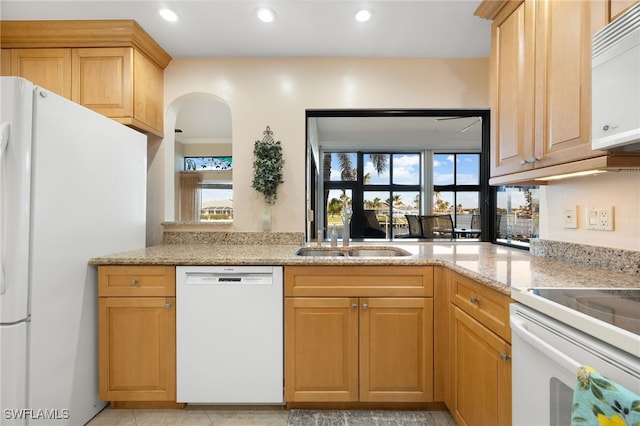 kitchen with light stone counters, white appliances, sink, and light brown cabinetry