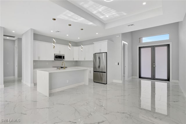 kitchen featuring french doors, stainless steel appliances, decorative light fixtures, a center island with sink, and white cabinets