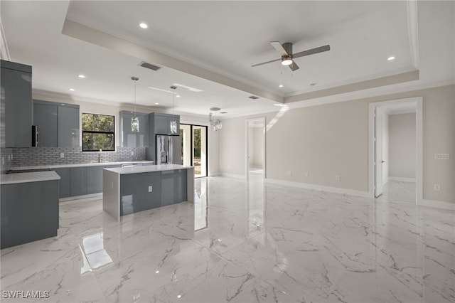 kitchen featuring ceiling fan with notable chandelier, a raised ceiling, hanging light fixtures, stainless steel fridge, and a kitchen island