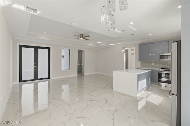 kitchen featuring a raised ceiling, appliances with stainless steel finishes, gray cabinets, a kitchen island, and ornamental molding