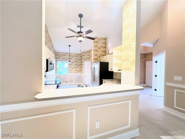 kitchen featuring kitchen peninsula, ceiling fan, light wood-type flooring, appliances with stainless steel finishes, and white cabinetry