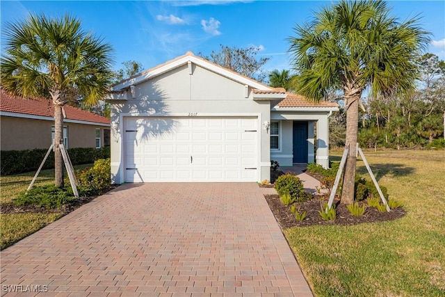 view of front of home featuring a garage, a tiled roof, decorative driveway, stucco siding, and a front lawn