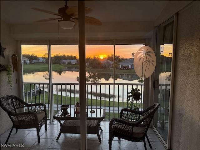 sunroom with ceiling fan and a water view