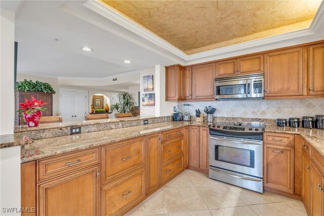 kitchen with appliances with stainless steel finishes, a tray ceiling, a peninsula, and light stone counters