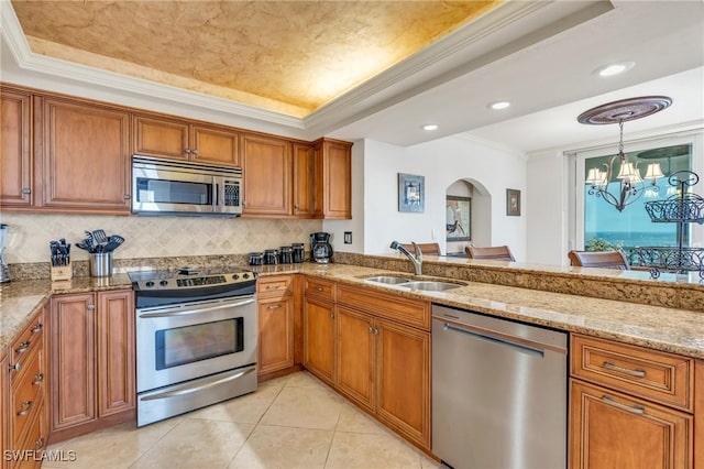 kitchen with light stone counters, a tray ceiling, appliances with stainless steel finishes, ornamental molding, and a sink