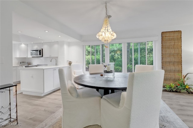 dining area with light hardwood / wood-style floors, sink, a wealth of natural light, and an inviting chandelier