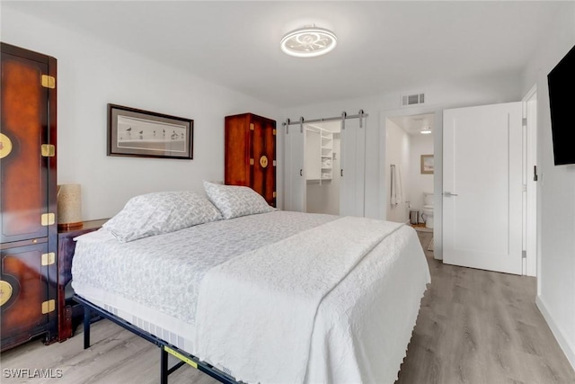 bedroom with a barn door, ensuite bathroom, and light hardwood / wood-style floors