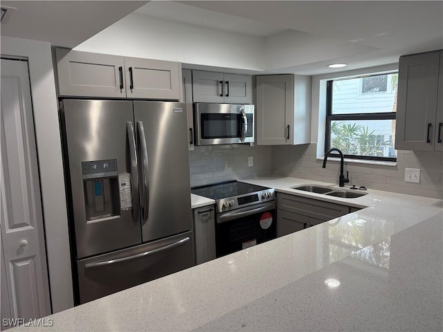 kitchen with backsplash, light stone counters, gray cabinetry, stainless steel appliances, and sink