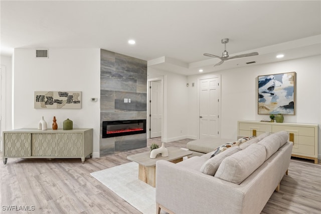 living room featuring light wood-type flooring, ceiling fan, and a tiled fireplace