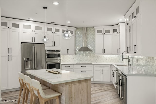 kitchen featuring light stone countertops, sink, wall chimney exhaust hood, a kitchen island, and appliances with stainless steel finishes