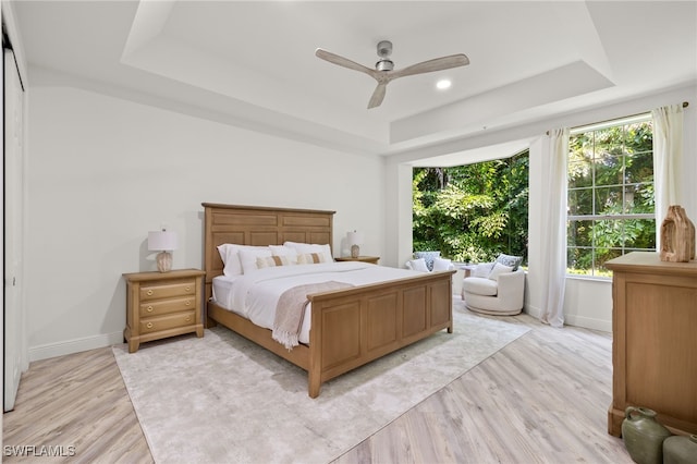 bedroom featuring a raised ceiling, a closet, ceiling fan, and light hardwood / wood-style flooring