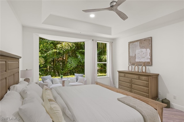 bedroom with ceiling fan, a raised ceiling, and light hardwood / wood-style flooring