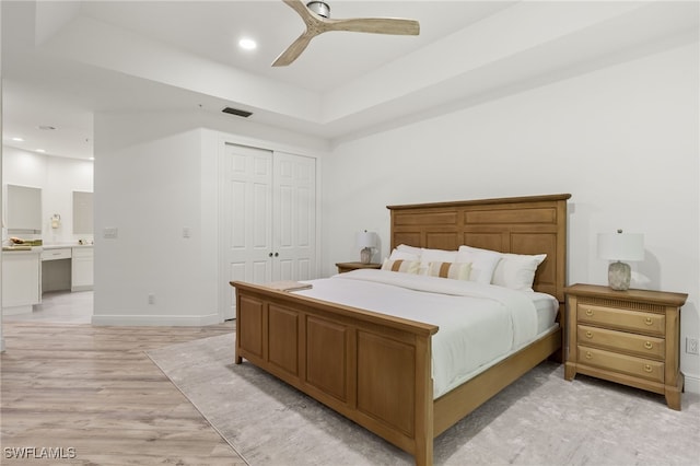 bedroom with a raised ceiling, a closet, light hardwood / wood-style flooring, and ceiling fan