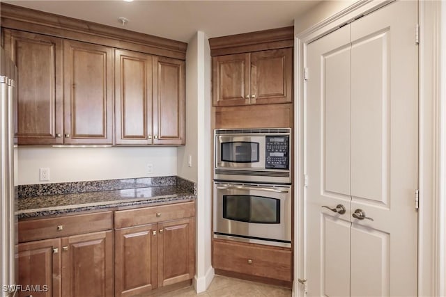 kitchen featuring light tile patterned floors, stainless steel appliances, and dark stone counters