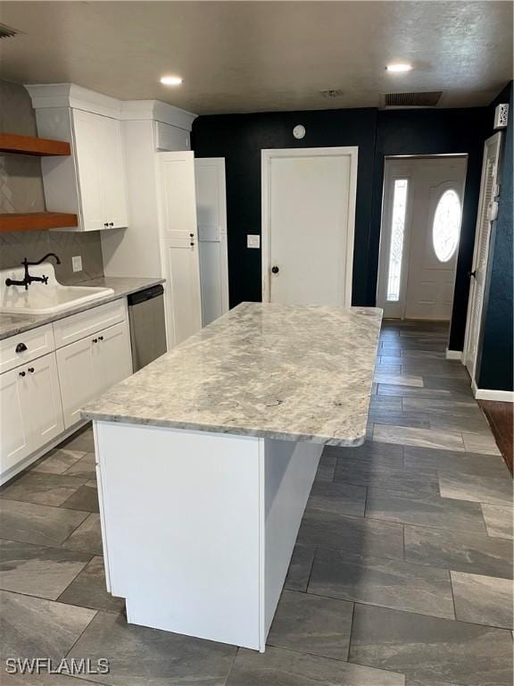 kitchen with tasteful backsplash, stainless steel dishwasher, sink, white cabinets, and a center island