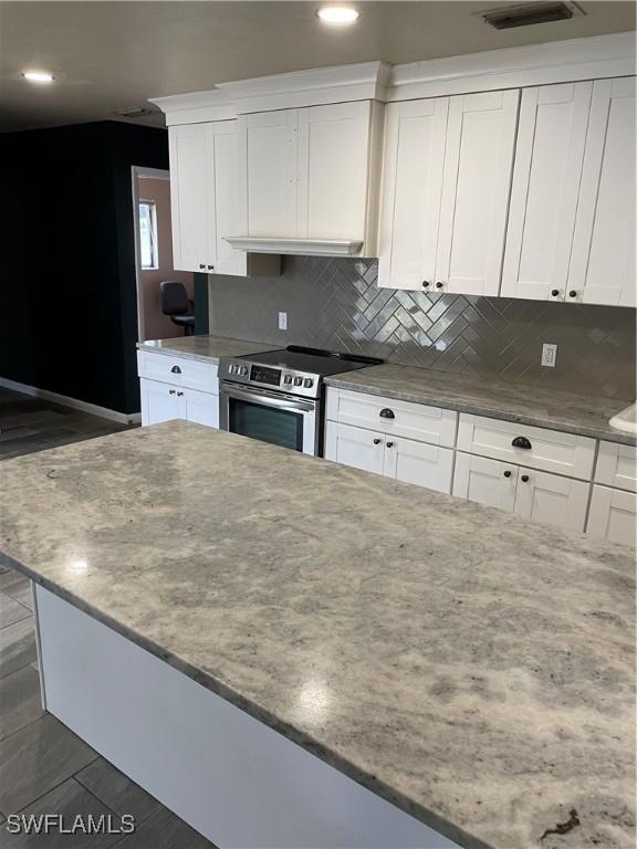 kitchen with stainless steel electric stove, light stone counters, white cabinetry, and tasteful backsplash