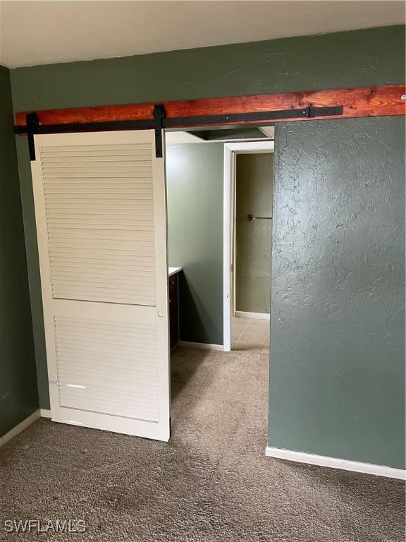 unfurnished bedroom with carpet flooring and a barn door