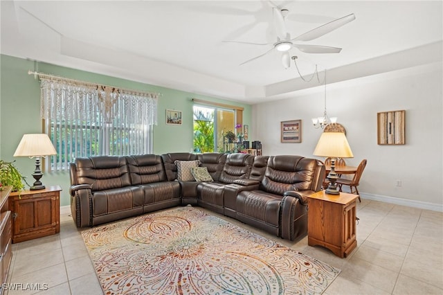 living room with a raised ceiling, ceiling fan with notable chandelier, and light tile patterned floors