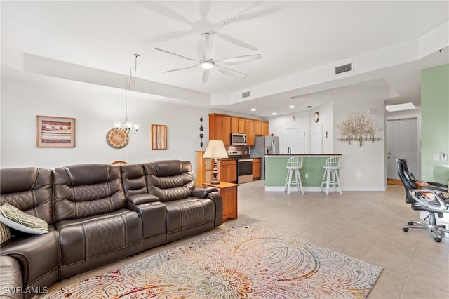 tiled living room featuring a tray ceiling and ceiling fan with notable chandelier