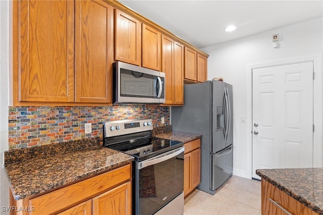 kitchen featuring light tile patterned flooring, appliances with stainless steel finishes, backsplash, and dark stone countertops