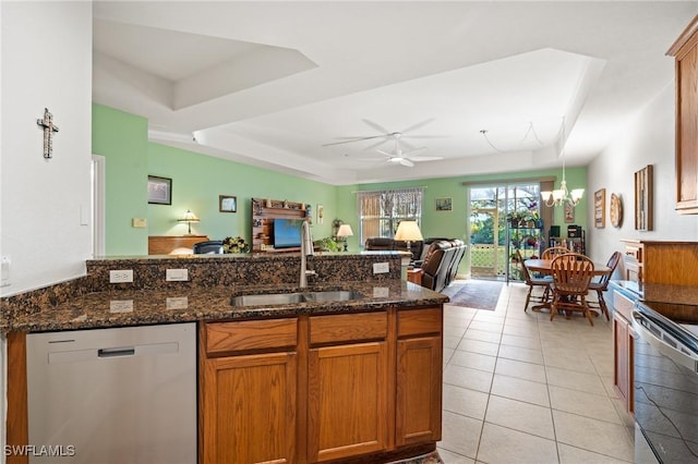 kitchen with ceiling fan with notable chandelier, dishwasher, sink, dark stone countertops, and a raised ceiling