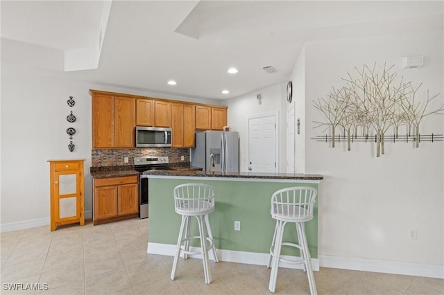 kitchen with tasteful backsplash, dark stone counters, a kitchen breakfast bar, stainless steel appliances, and a kitchen island with sink