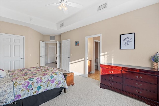 bedroom featuring a raised ceiling, ensuite bathroom, light carpet, and ceiling fan