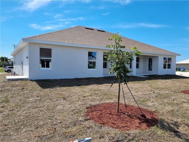 back of property featuring a shingled roof, a lawn, and stucco siding