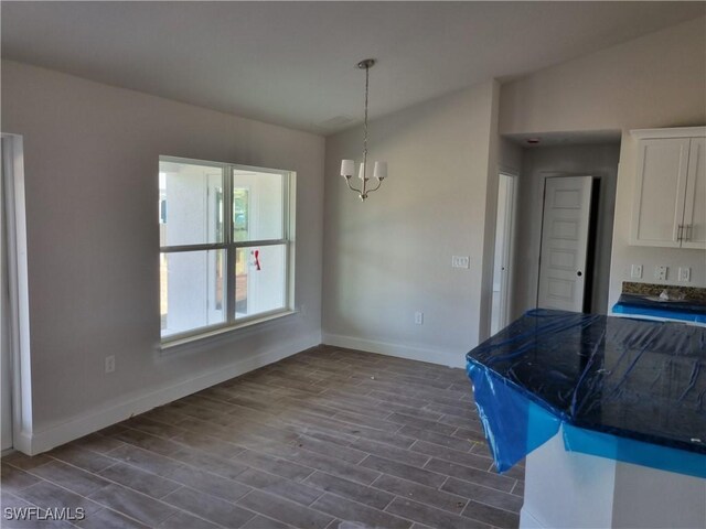 unfurnished dining area featuring lofted ceiling, baseboards, a chandelier, and dark wood-type flooring