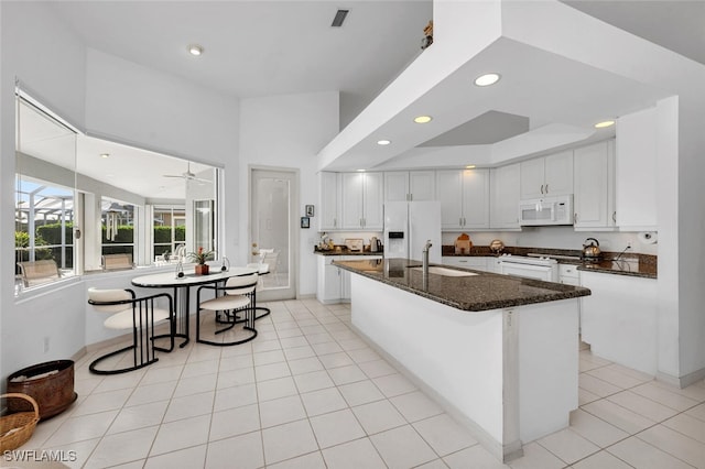 kitchen featuring white appliances, a kitchen island with sink, dark stone counters, sink, and white cabinetry