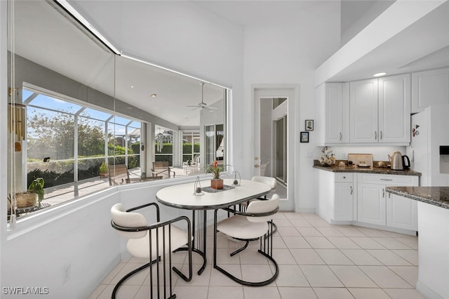 kitchen featuring ceiling fan, light tile patterned floors, white refrigerator, dark stone countertops, and white cabinets