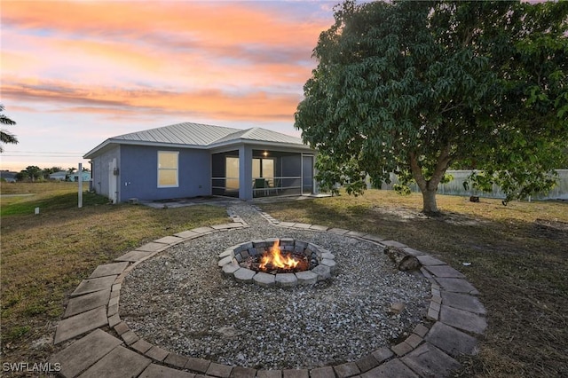 back house at dusk featuring a lawn, a sunroom, and a fire pit