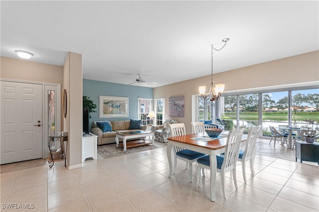 tiled dining room with ceiling fan with notable chandelier and a water view