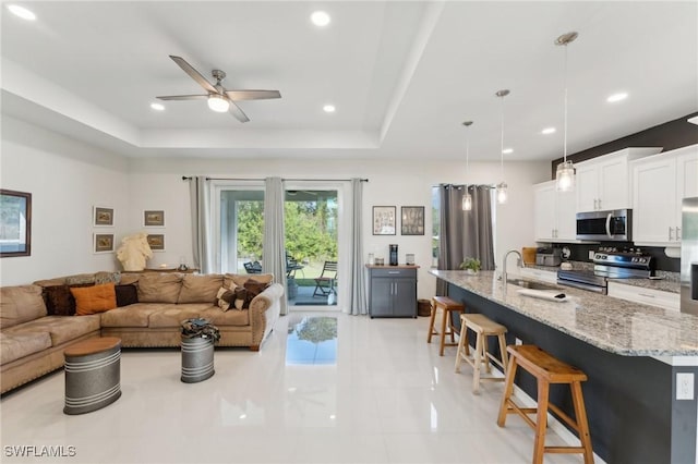 tiled living room featuring ceiling fan, sink, and a tray ceiling