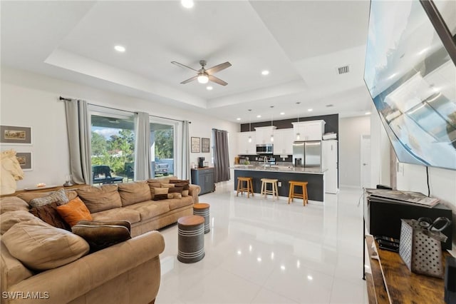 tiled living room featuring ceiling fan and a tray ceiling